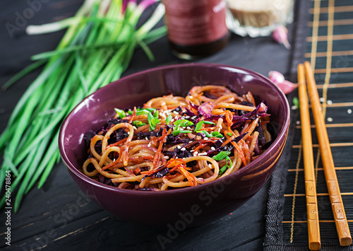 Chinese food. Vegan stir fry noodles with red cabbage and carrot in a bowl on a black wooden background. Asian cuisine meal.