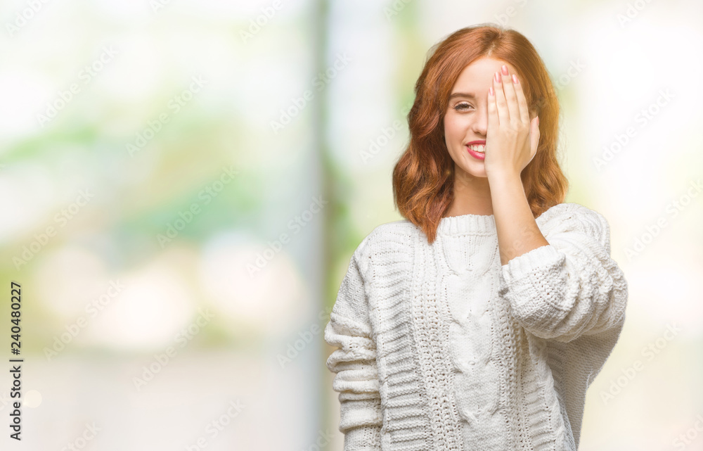 Young beautiful woman over isolated background wearing winter sweater covering one eye with hand with confident smile on face and surprise emotion. Young beautiful woman over isolated background wearing winter sweater covering one eye with hand with confident smile on face and surprise emotion.