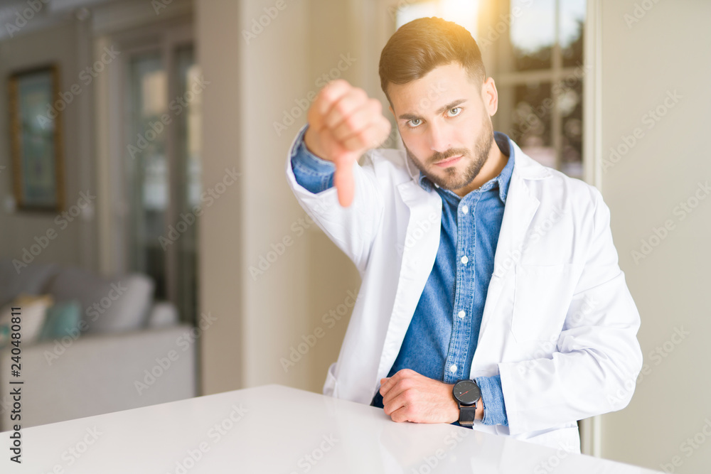 Young handsome doctor man at the clinic looking unhappy and angry showing rejection and negative with thumbs down gesture. Bad expression.