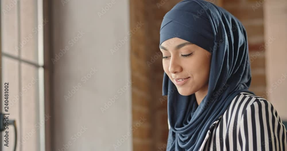 Young muslim woman wearing hijab sitting in modern cafe, working, searching or studying at her laptop, then looking at camera - modern muslim concept closeup 4k Young muslim woman wearing hijab sitting in modern cafe, working, searching or studying at her laptop, then looking at camera - modern muslim concept closeup 4k