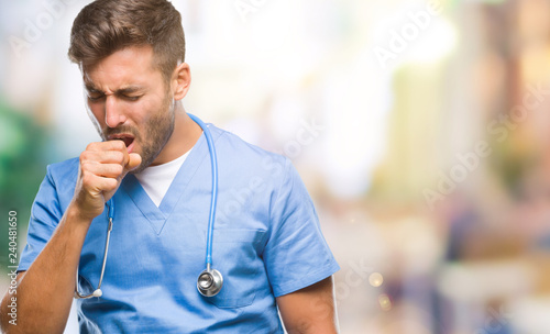 Young handsome doctor surgeon man over isolated background feeling unwell and coughing as symptom for cold or bronchitis. Healthcare concept.