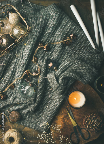 Christmas or New Year holiday festive mood. Flat-lay of grey warm woolen winter sweater, candles, led garland and vintage stylish Christrmas decoration toys over dark wood rustic table background photo