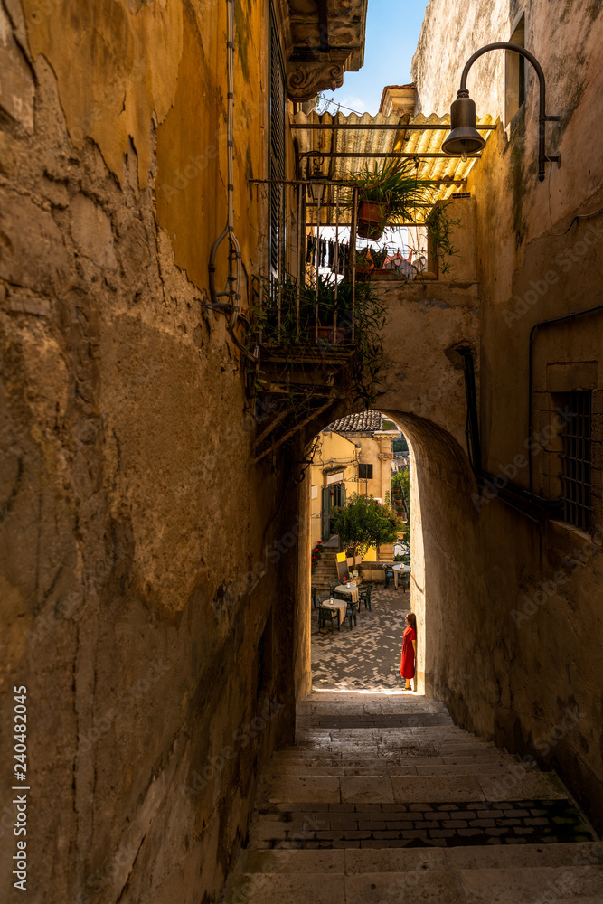 Girl stands under the arch in the old baroque town Modica in Sicily, Italy