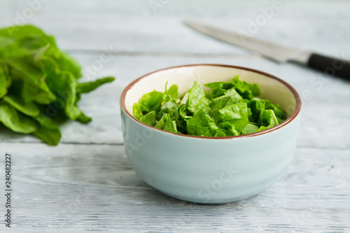 bunch of green sorrel leaves and a bowl of sliced salad on a wooden table