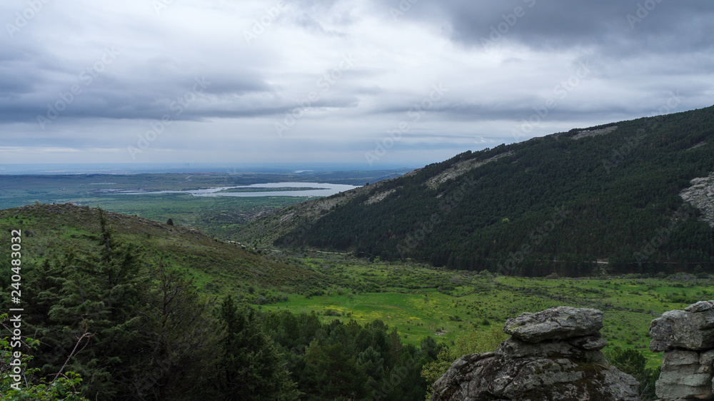 landscape of a mountainous valley with a lake in the background on a cloudy spring day