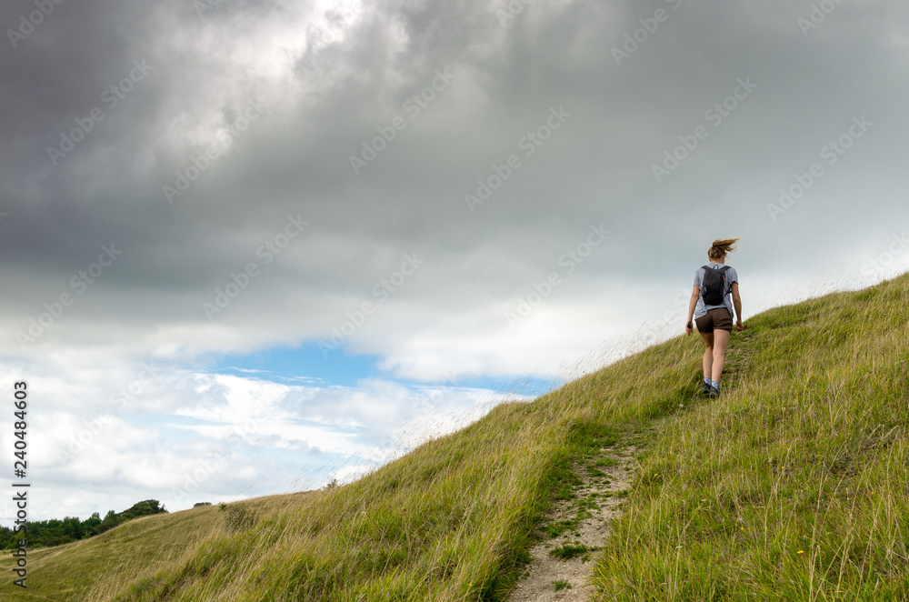 Young woman hiking in the countryside on a windy summer’s day. Photo taken in the Cotswold Way, England