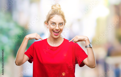 Fototapeta Naklejka Na Ścianę i Meble -  Young beautiful blonde woman wearing red t-shirt and glasses over isolated background looking confident with smile on face, pointing oneself with fingers proud and happy.