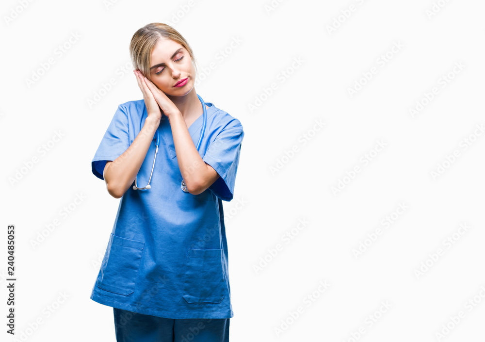 Young beautiful blonde doctor surgeon nurse woman over isolated background sleeping tired dreaming and posing with hands together while smiling with closed eyes. Young beautiful blonde doctor surgeon nurse woman over isolated background sleeping tired dreaming and posing with hands together while smiling with closed eyes.