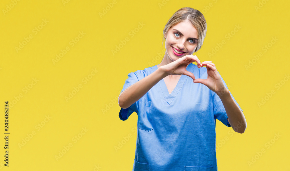 Fototapeta premium Młoda piękna blondynka lekarz chirurg pielęgniarka kobieta na białym tle uśmiechając się w miłości pokazując symbol serca i kształt rękami. Romantyczna koncepcja.