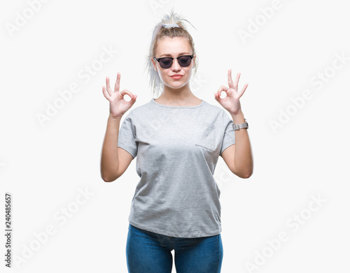 Young blonde woman wearing sunglasses over isolated background relax and smiling with eyes closed doing meditation gesture with fingers. Yoga concept.