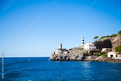 lighthouse on a background of blue clear water, mountains and rocks. the mediterranean