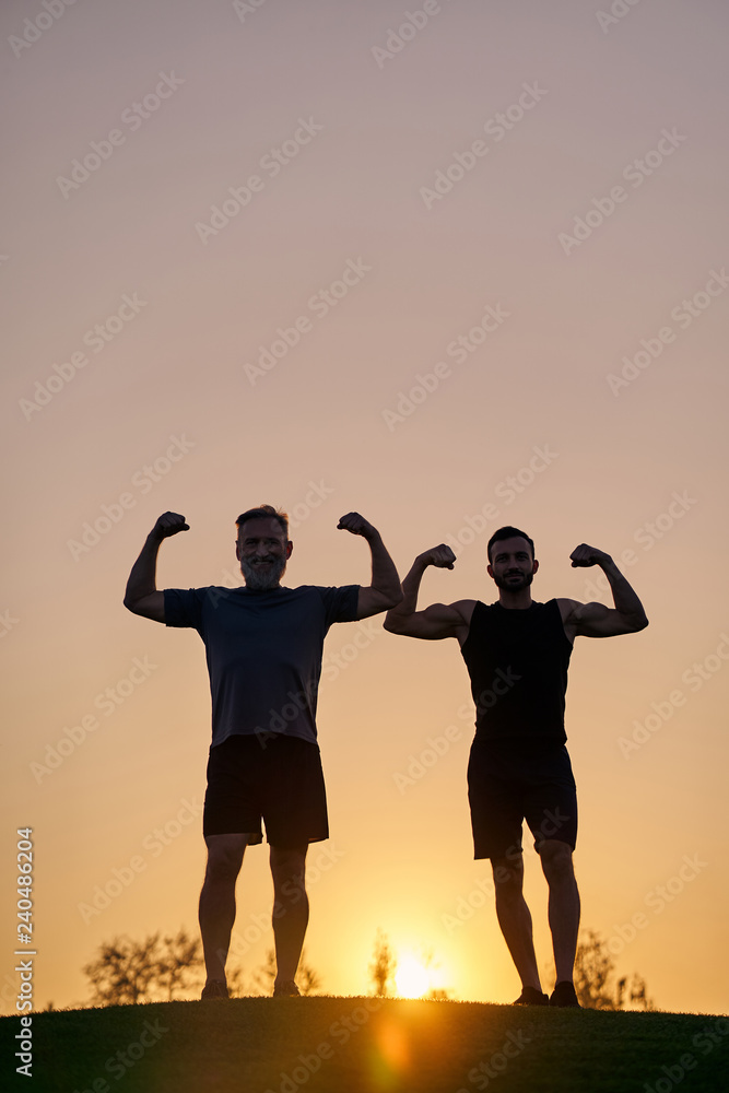 The two sportsmen show muscles on the sunset background