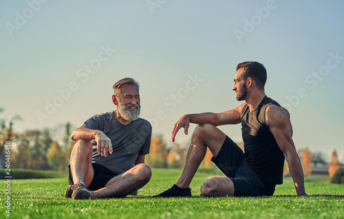 The old and young sportsmen sitting on the grass