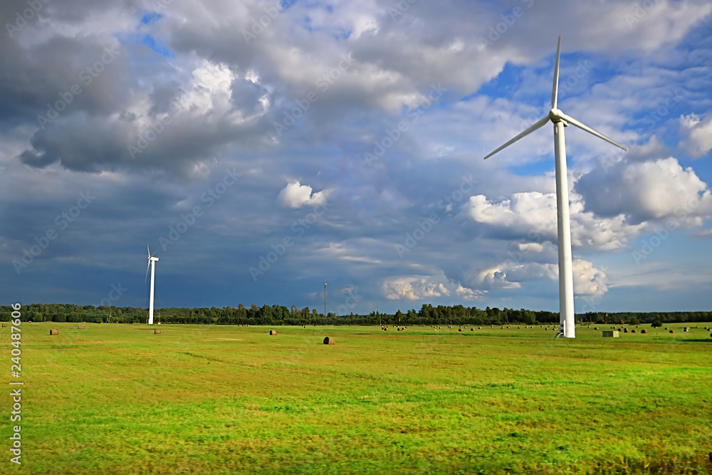 Wind generators turbines on summer landscape, blue sky, green grass and corps field, rainy weather, Latvia Wind generators turbines on summer landscape, blue sky, green grass and corps field, rainy weather, Latvia
