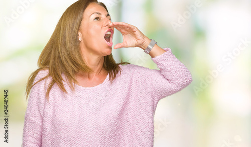 Beautiful middle age adult woman wearing winter sweater over isolated background shouting and screaming loud to side with hand on mouth. Communication concept.