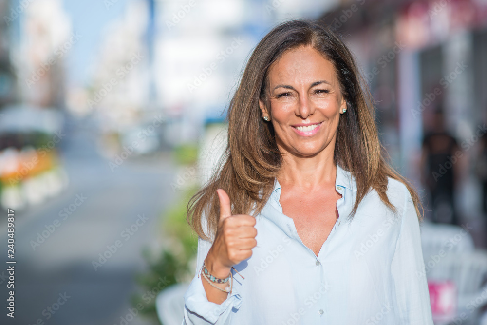Beautiful middle age hispanic woman at the city street on a sunny day happy with big smile doing ok sign, thumb up with fingers, excellent sign Beautiful middle age hispanic woman at the city street on a sunny day happy with big smile doing ok sign, thumb up with fingers, excellent sign