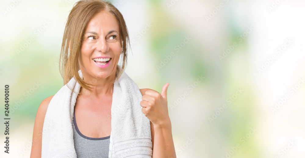 Beautiful middle age woman wearing sport clothes and a towel over isolated background smiling with happy face looking and pointing to the side with thumb up.