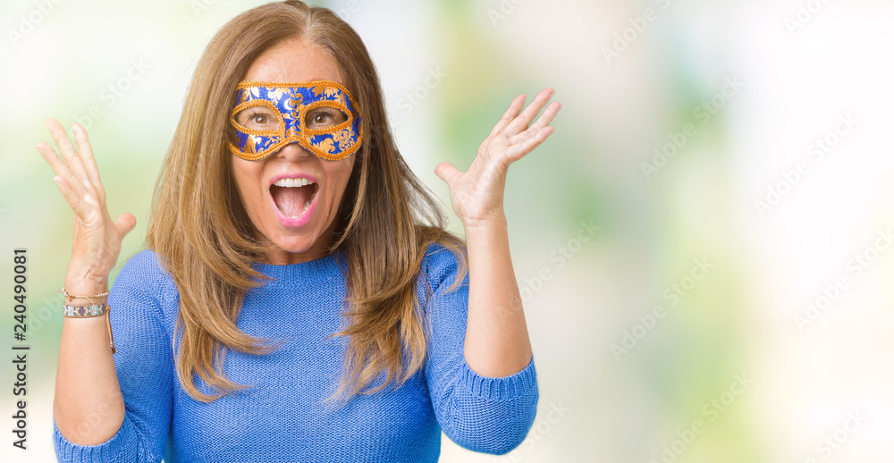Beautiful middle age woman wearing venice carnival mask over isolated background celebrating crazy and amazed for success with arms raised and open eyes screaming excited. Winner concept Beautiful middle age woman wearing venice carnival mask over isolated background celebrating crazy and amazed for success with arms raised and open eyes screaming excited. Winner concept