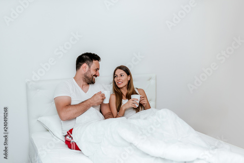 Weekend concept. Couple in the bed holding mugs.