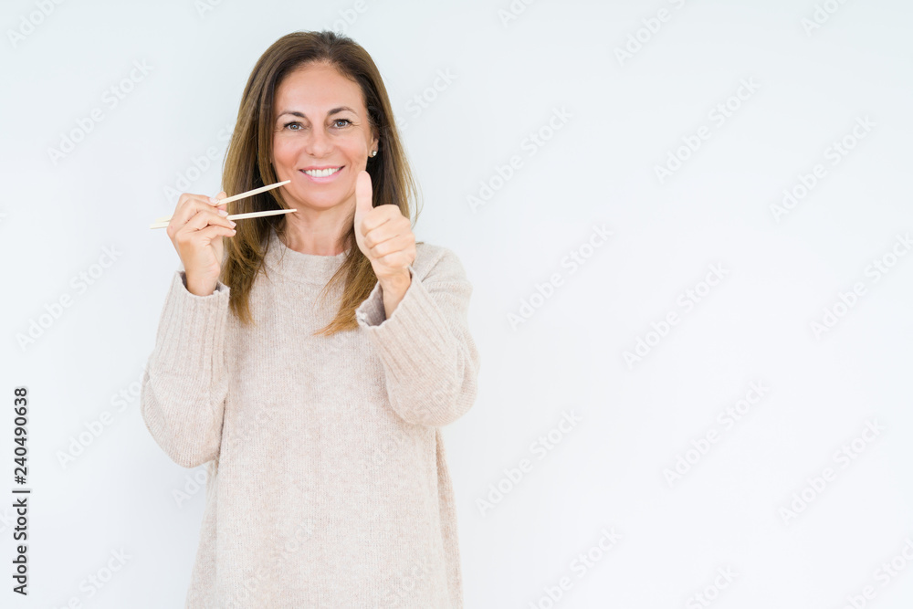 Middle age woman holding asian chopsticks over isolated background happy with big smile doing ok sign, thumb up with fingers, excellent sign Middle age woman holding asian chopsticks over isolated background happy with big smile doing ok sign, thumb up with fingers, excellent sign