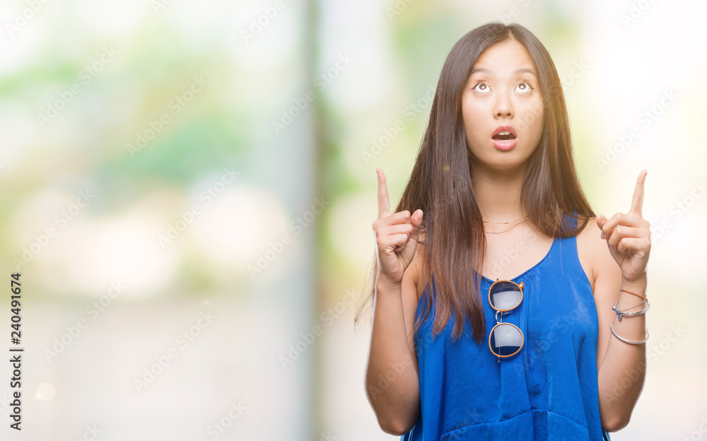 Young asian woman over isolated background amazed and surprised looking up and pointing with fingers and raised arms. Young asian woman over isolated background amazed and surprised looking up and pointing with fingers and raised arms.