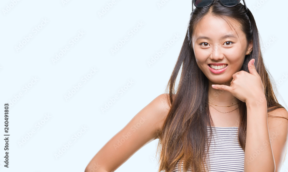 Young asian woman wearing sunglasses over isolated background smiling doing phone gesture with hand and fingers like talking on the telephone. Communicating concepts. Young asian woman wearing sunglasses over isolated background smiling doing phone gesture with hand and fingers like talking on the telephone. Communicating concepts.