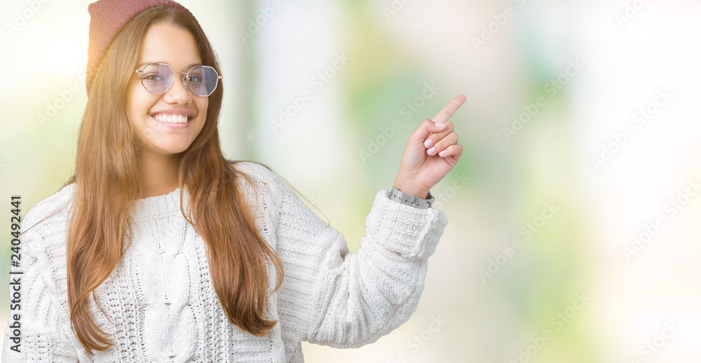 Young beautiful brunette hipster woman wearing sunglasses over isolated background with a big smile on face, pointing with hand and finger to the side looking at the camera.