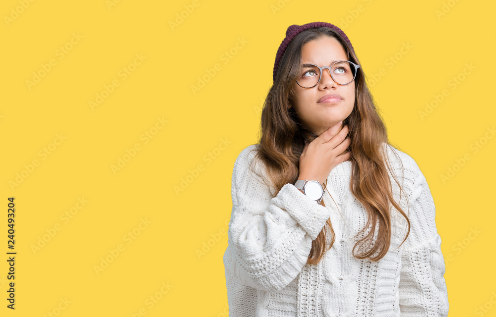 Young beautiful brunette hipster woman wearing glasses and winter hat over isolated background Touching painful neck, sore throat for flu, clod and infection Young beautiful brunette hipster woman wearing glasses and winter hat over isolated background Touching painful neck, sore throat for flu, clod and infection