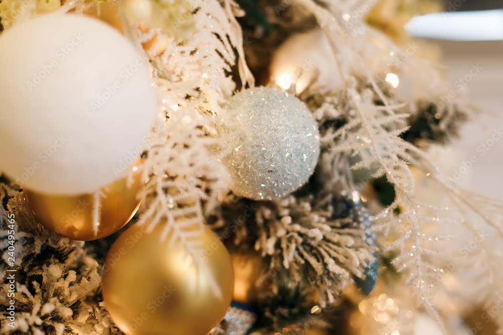 Fototapeta premium Close-photographed Christmas decorations on a gold and white Christmas tree with sparkles. Christmas decor elements