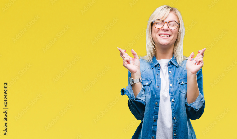 Young beautiful blonde woman wearing glasses over isolated background smiling crossing fingers with hope and eyes closed. Luck and superstitious concept. Young beautiful blonde woman wearing glasses over isolated background smiling crossing fingers with hope and eyes closed. Luck and superstitious concept.