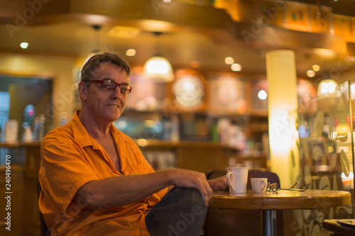 Man holding mug of coffee with a smile enjoying life in a Cafe wearing a orange shirt