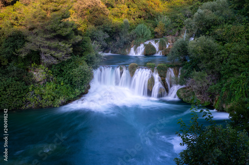 Waterfall at Krka, Croatia surrounded by green trees. Dark blue water.