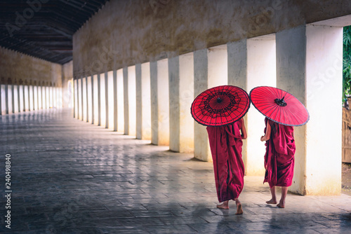 Billede på lærred Two buddhist monk novice holding red umbrellas and walking in pagoda, Myanmar