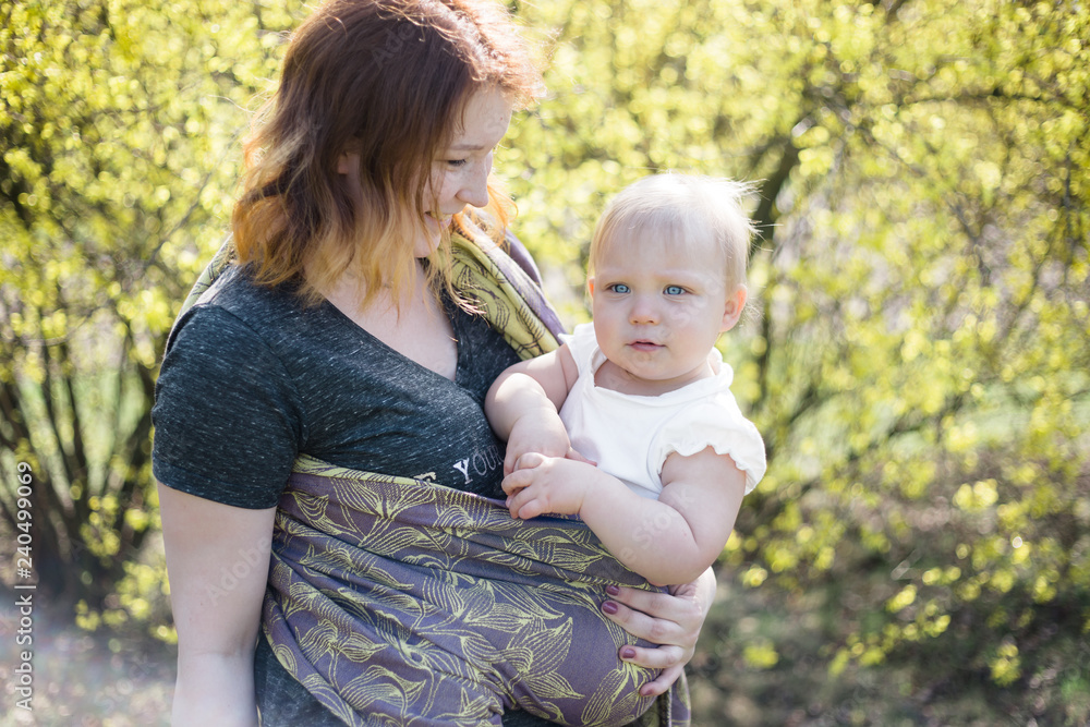 Mother holding her daughter wrapped in a purple sling, looking at her lovingly. Sunny, lifestyle, high key capture. Mother holding her daughter wrapped in a purple sling, looking at her lovingly. Sunny, lifestyle, high key capture.