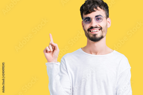 Young handsome man wearing sunglasses over isolated background with a big smile on face, pointing with hand and finger to the side looking at the camera.