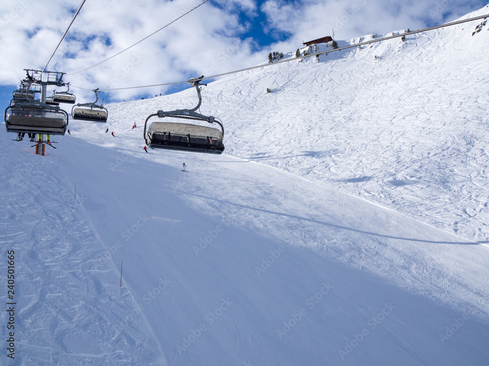 Chairs of ski-lift in the ski resort in the early morning at dawn with mountain peak in the distance. Winter snowboard and skiing concept. France, Courchevel, 2018