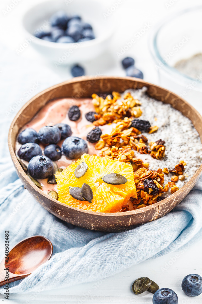 Breakfast smoothie bowl with chia pudding, berries and granola in a coconut shell on white wooden background. Breakfast smoothie bowl with chia pudding, berries and granola in a coconut shell on white wooden background.
