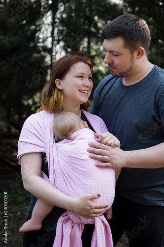 Young parents with baby in a sling. Modern babywearing trend.