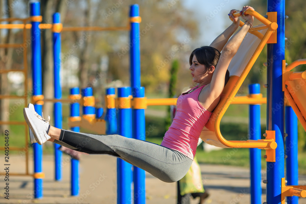 Young athletic girl in a pink t-shirt doing press exercises on the street sports ground in the park in the autumn.