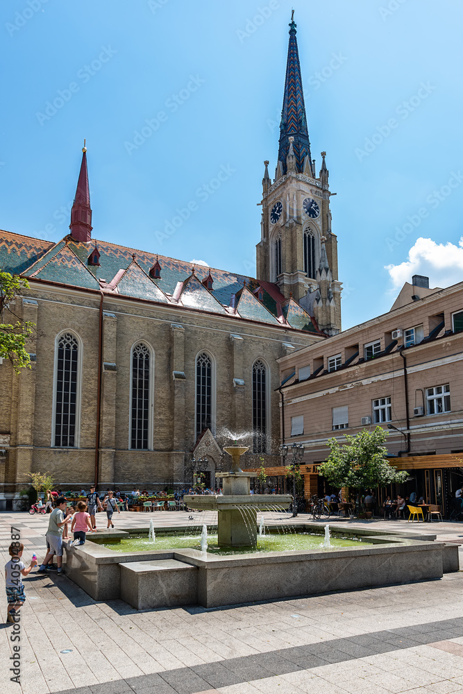 Fototapeta premium Novi Sad, Serbia - May 27, 2018: View of one square with fountain and old buildings located behind at the Catholic Church `The Name of Mary Church