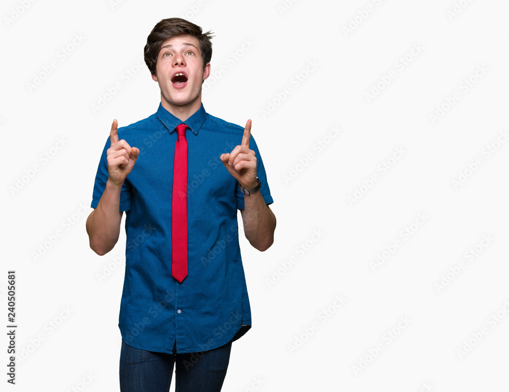 Young handsome business man wearing red tie over isolated background amazed and surprised looking up and pointing with fingers and raised arms.