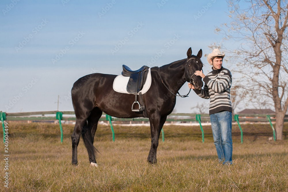 Man nearby horse, striped pullover, blue jeans, hat, landscape Man nearby horse, striped pullover, blue jeans, hat, landscape