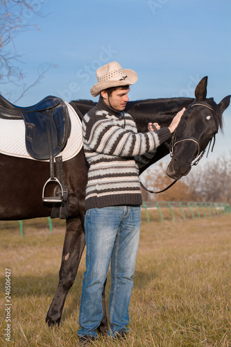 Man nearby horse, striped pullover, blue jeans, hat, landscape