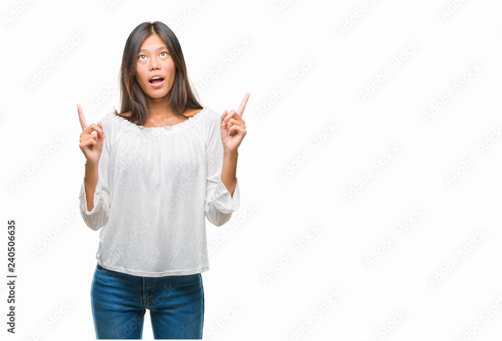 Young asian woman over isolated background amazed and surprised looking up and pointing with fingers and raised arms. Young asian woman over isolated background amazed and surprised looking up and pointing with fingers and raised arms.