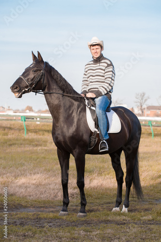 Man riding horse, striped pullover, blue jeans, hat, landscape