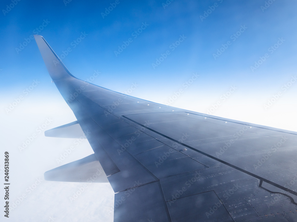 view of airplane wing in blue sky over clouds