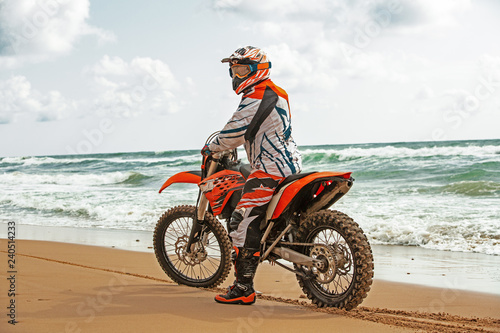 Motorcyclist in a protective suit sitting on motorbike in front of the sea