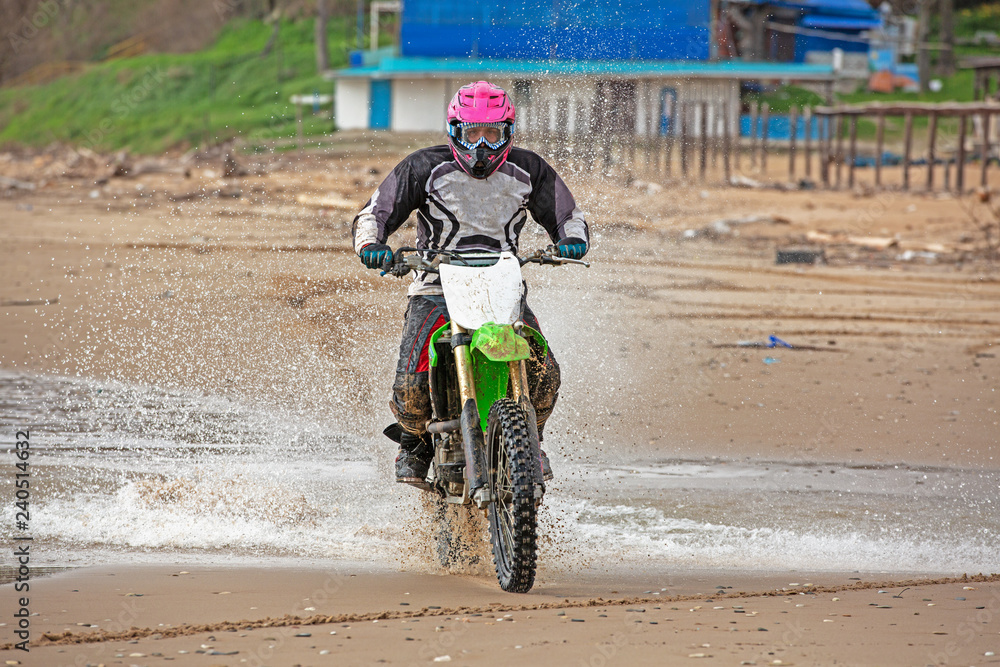 Obraz premium Motorcyclist in a protective suit rides a motorcycle on the sea, splashes fly from under the wheels.