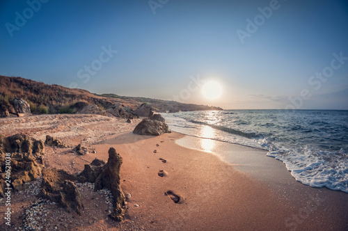 Beautiful landscape, rocky sea bay at sunset with footprints in the sand