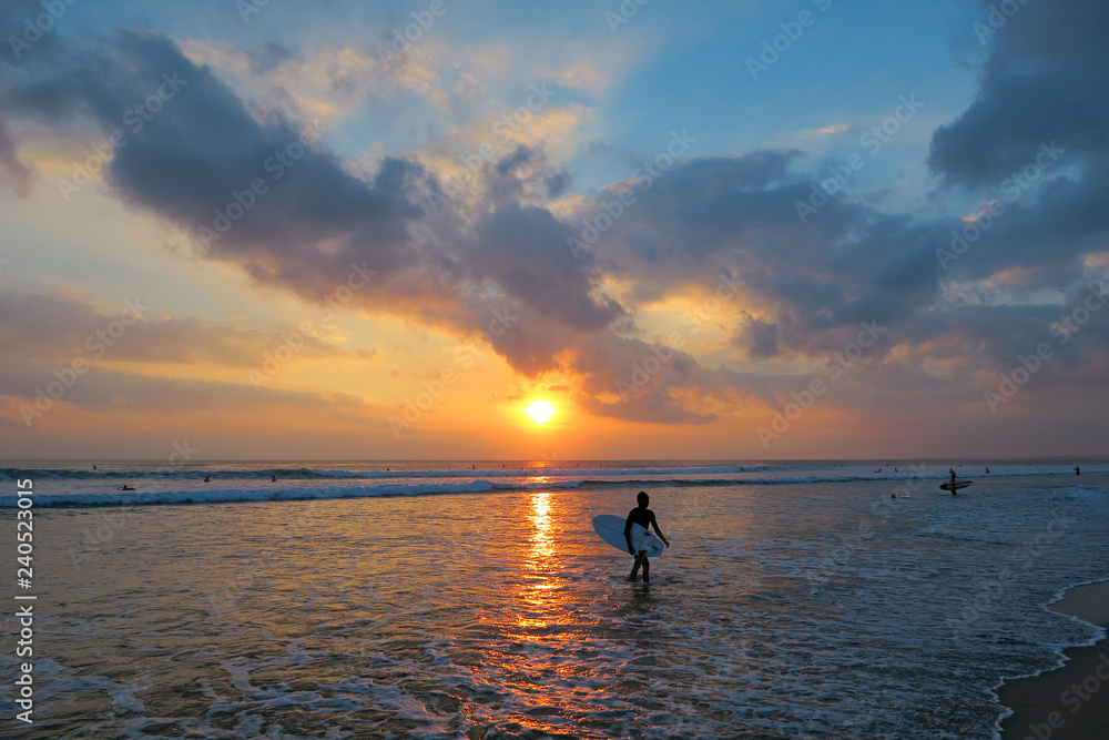 Young surfer silhouette with surfboard at beautiful sunset background, Kuta beach, Bali, Indonesia